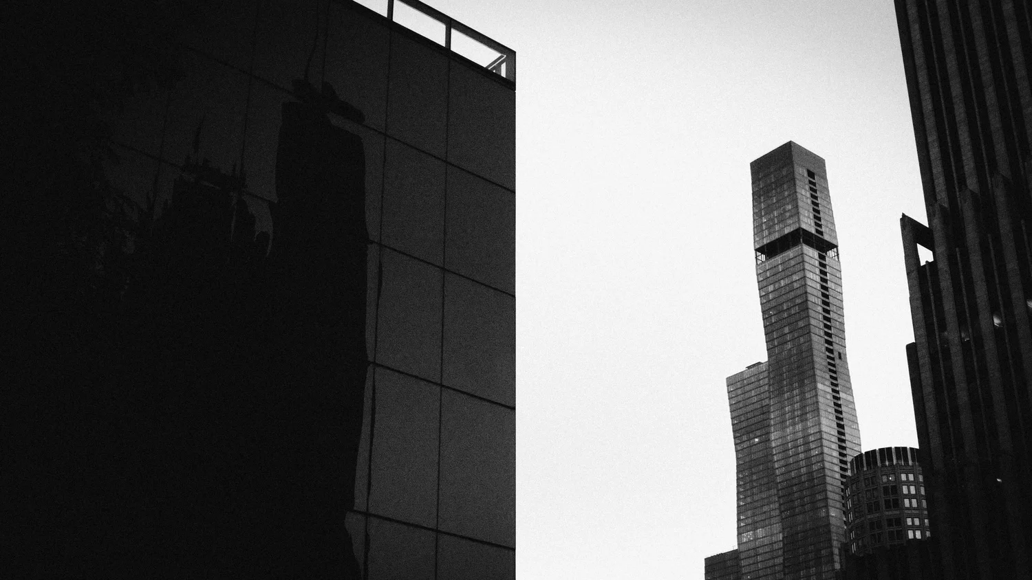 High-contrast black and white photo of a dark building edge against a bright blank sky next to a tall tiered skyscraper