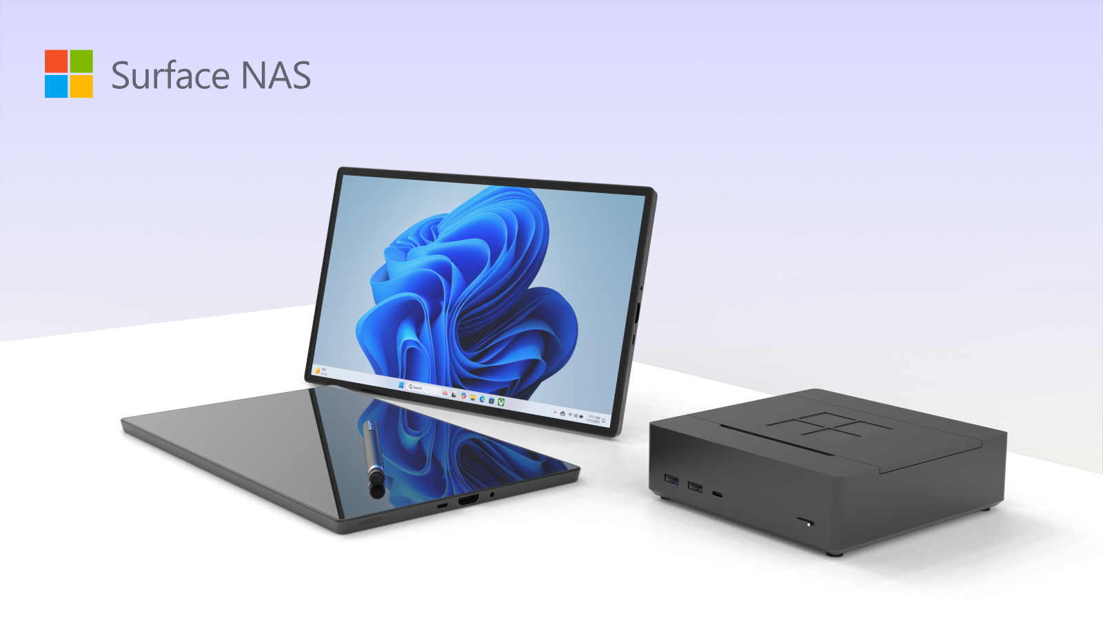 The Microsoft Surface NAS, a low dark grey box with a four pane logo on its lid, standing beside a Surface tablet showing a blue Windows wallpaper.