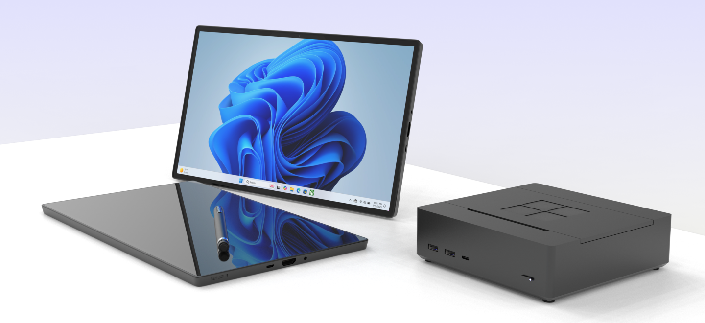 The Microsoft Surface NAS, a low dark grey box with a four pane logo on its lid, standing beside a Surface tablet showing a blue Windows wallpaper.